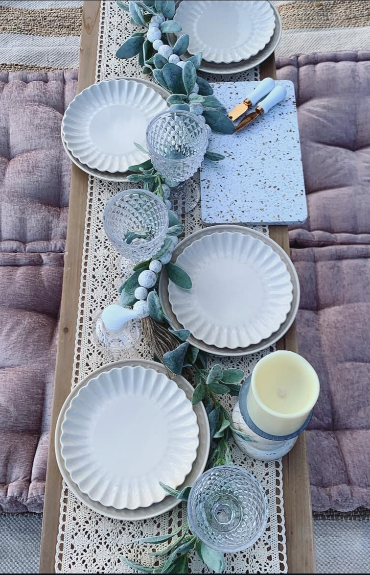 Close view of a styled picnic table with lace runner, scalloped plates, and tufted rose cushions.