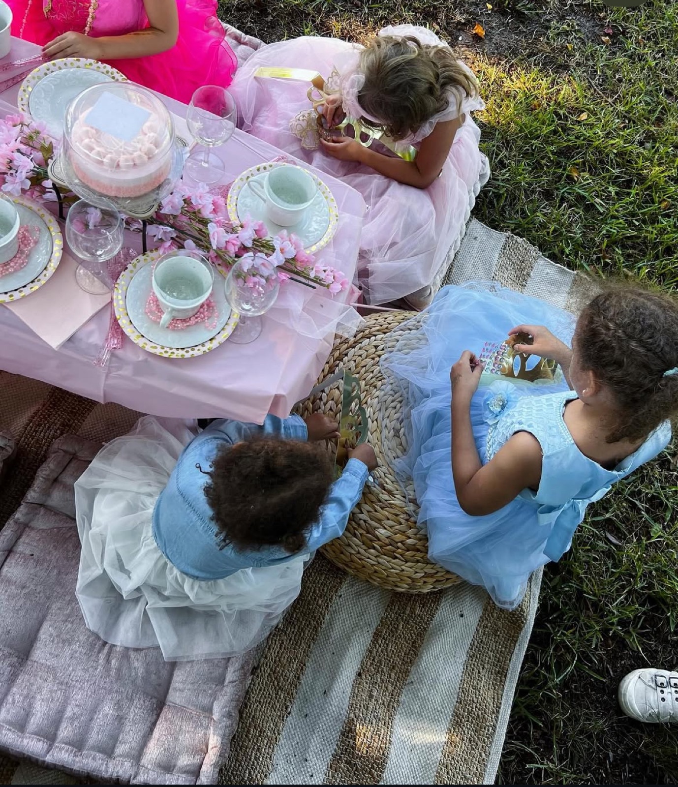Girls in party dresses around a pink low table with blossom branches and a dome cake.