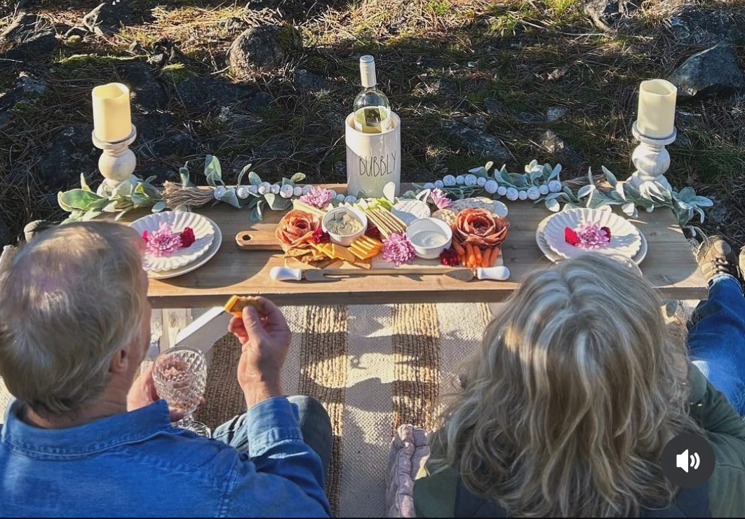 A couple at a styled picnic with a charcuterie board, pillar candles, and crystal glasses in late light.